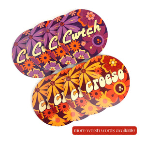 Colourful round coasters with floral patterns and Welsh words on a white background