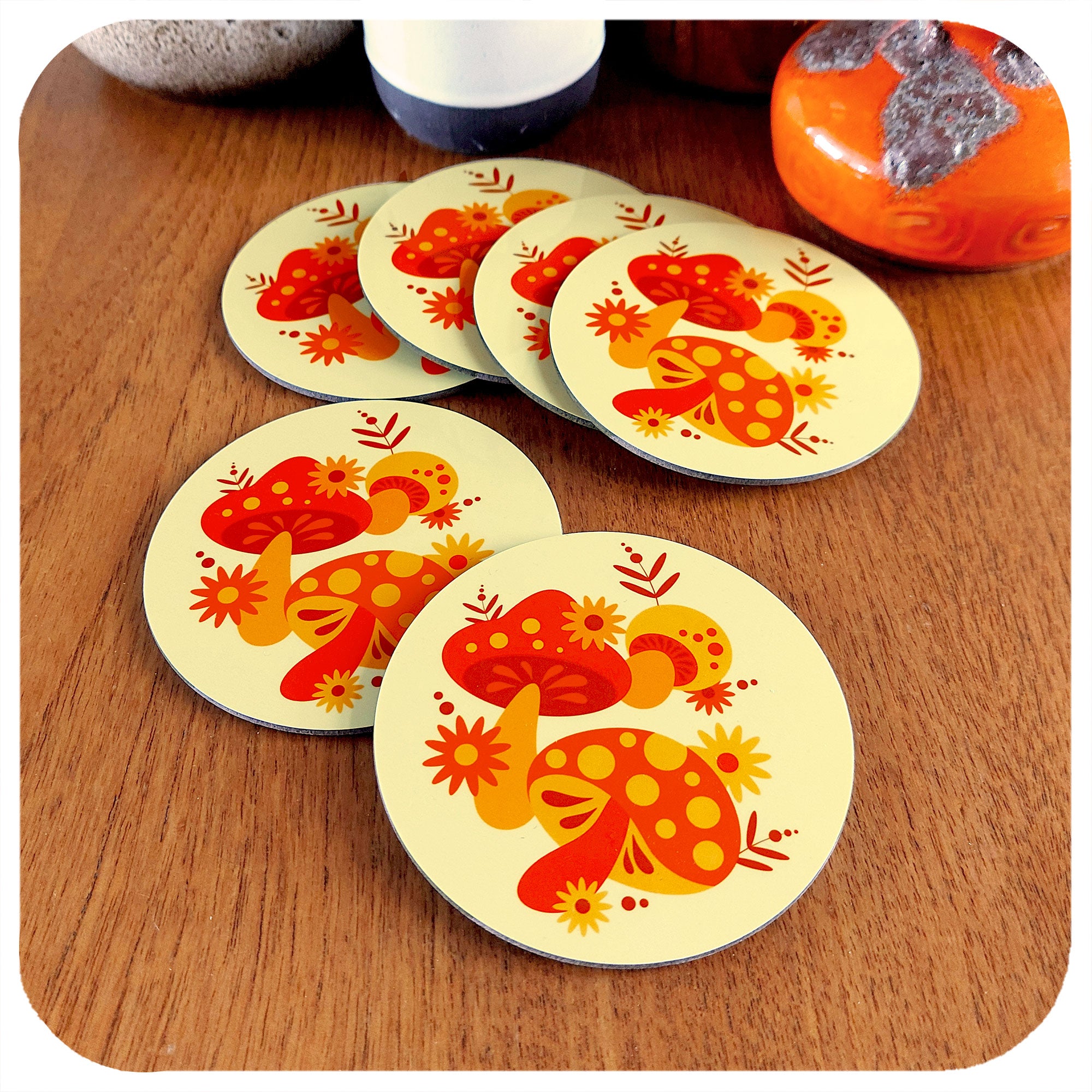 Set of 6 70s style retro coasters featuring orange, red & yellow mushrooms. They are lying on a teak next to a couple of vintage pottery piece.| The Inkabilly Emporium