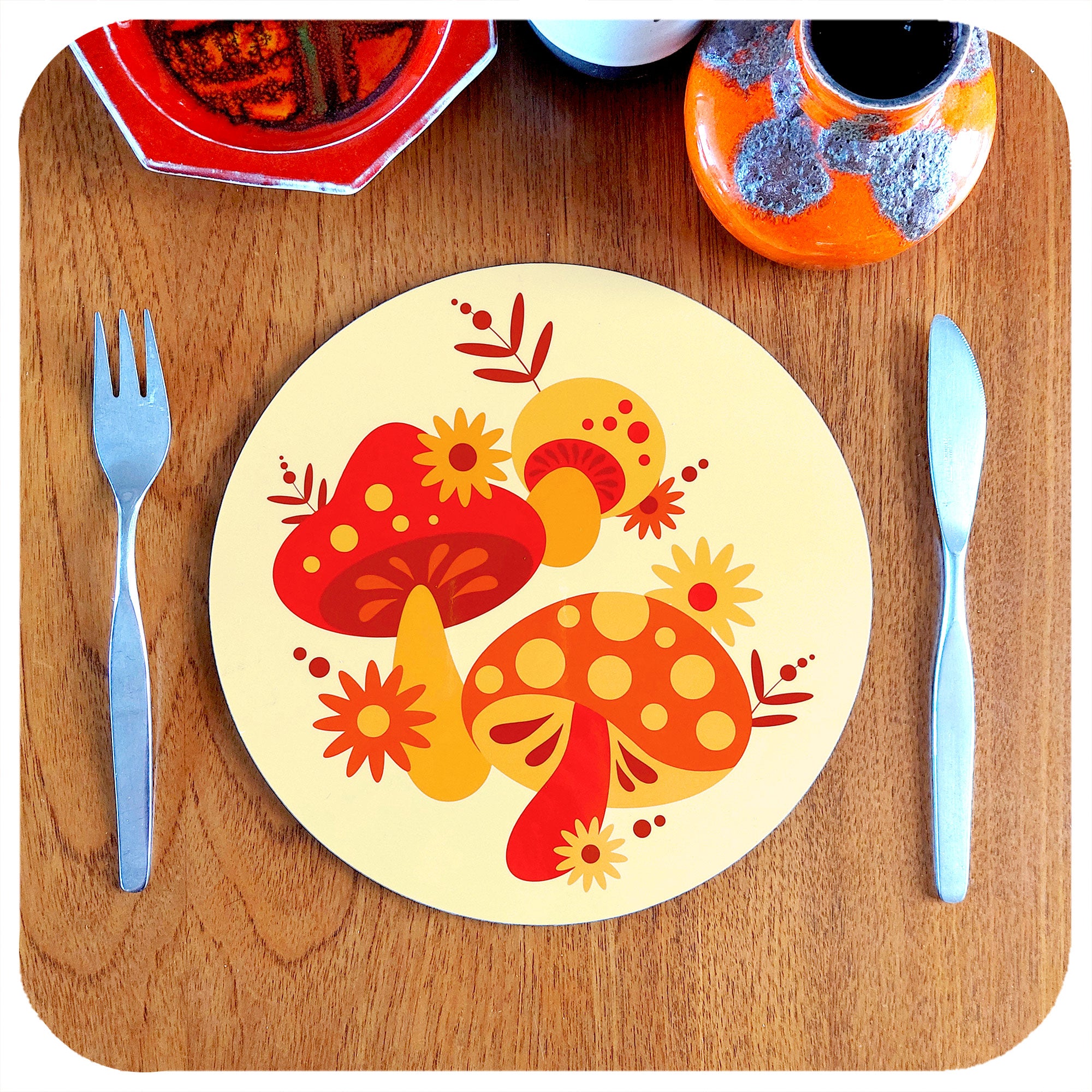 Retro Mushrooms Round Placemat sits on a teak table with knife and fork, plus vintage pottery pieces | The Inkabilly Emporium