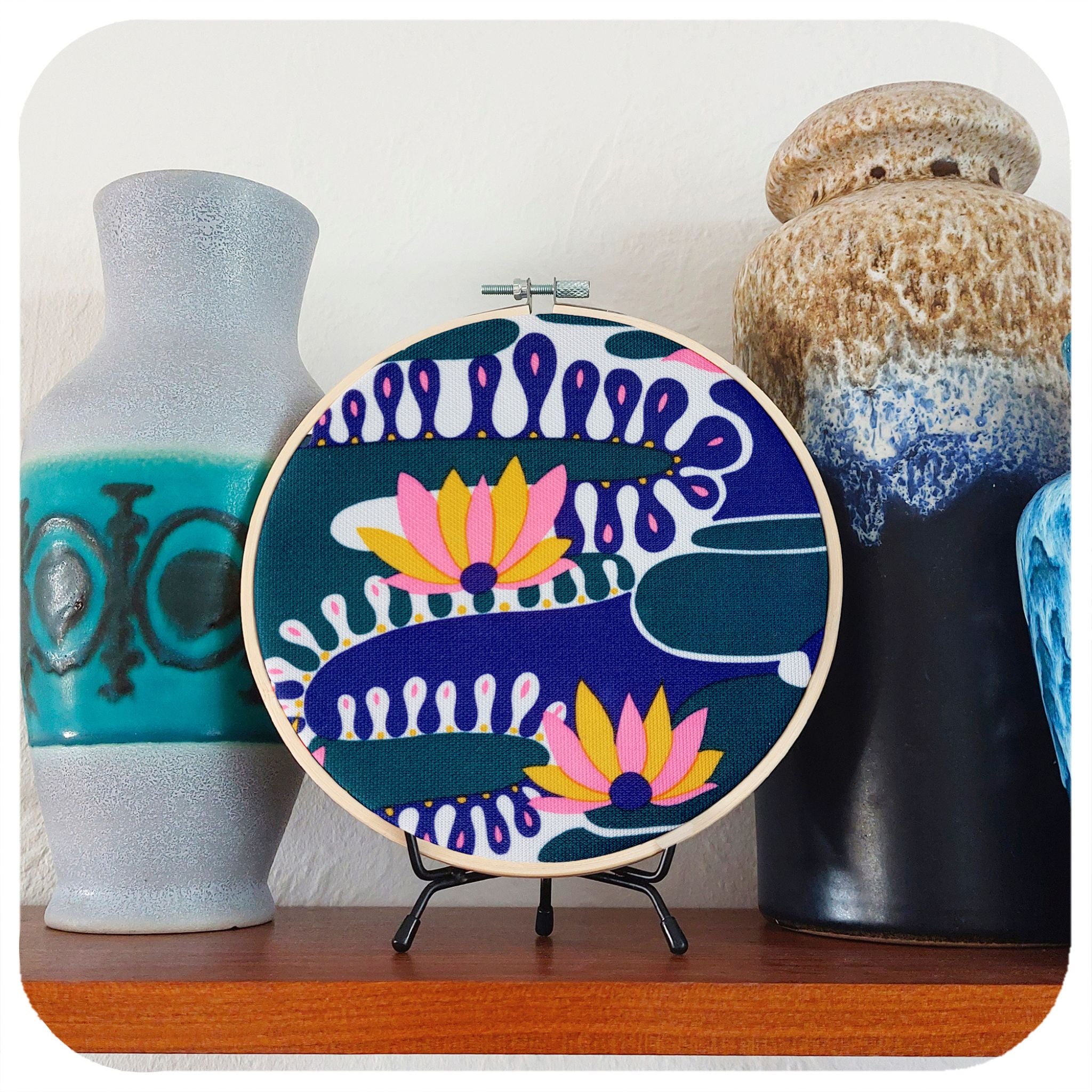 A framed vintage fabric hoop featuring psychedelic water lilies sits on a shelf with fat lava vases | The Inkabilly Emporium