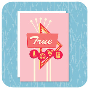 A pink A6 greetings card featuring a graphic rendering of a 50s style American roadside neon sign with the words "True Love" with a white envelope sits on a  textured light blue background | The Inkabilly Emporium