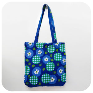 Blue tote bag with green and white pattern, of gingham and daisies, on a white background
