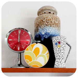 A framed vintage fabric hoop is displayed on a shelf with vintage pottery and a vintage clock | The Inkabilly Emporium