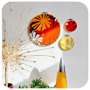  Three framed vintage fabric hoops hang on a white wall, in the foreground is a giant dried allium flower head and the top of a lava lamp | The Inkabilly Emporium