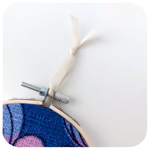 Close up of the ribbon hanging loop on a framed fabric hoop featuring a midcentury barkcloth floral design in lilac and blue | The Inkabilly Emporium