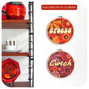 Colourful round wall decor pieces featuring welsh words, on a white wall next to a shelf