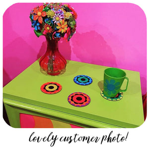Customer photo of flower power style coasters sitting on a bright green cupboard with a green mug and vase of flowers made from vintage brooches. Text along the bottom of the image reads : Lovely customer photo! | The Inkabilly Emporium