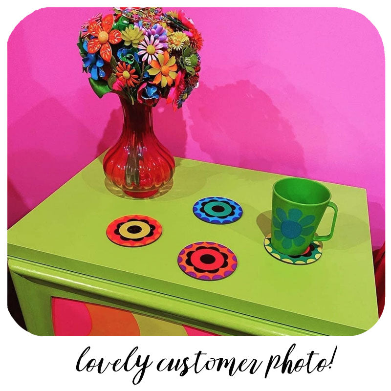 Customer photo of flower power style coasters sitting on a bright green cupboard with a green mug and vase of flowers made from vintage brooches. Text along the bottom of the image reads : Lovely customer photo! | The Inkabilly Emporium