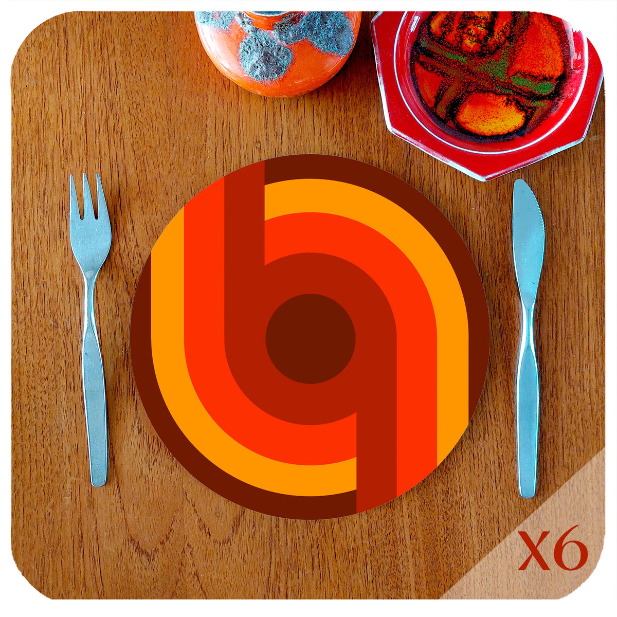 A 70s style round placemat lies on a teak table with vintage mid century knife and fork, and 2 mid century pottery pieces. text in the corner reads "X6" | The Inkabilly Emporium
