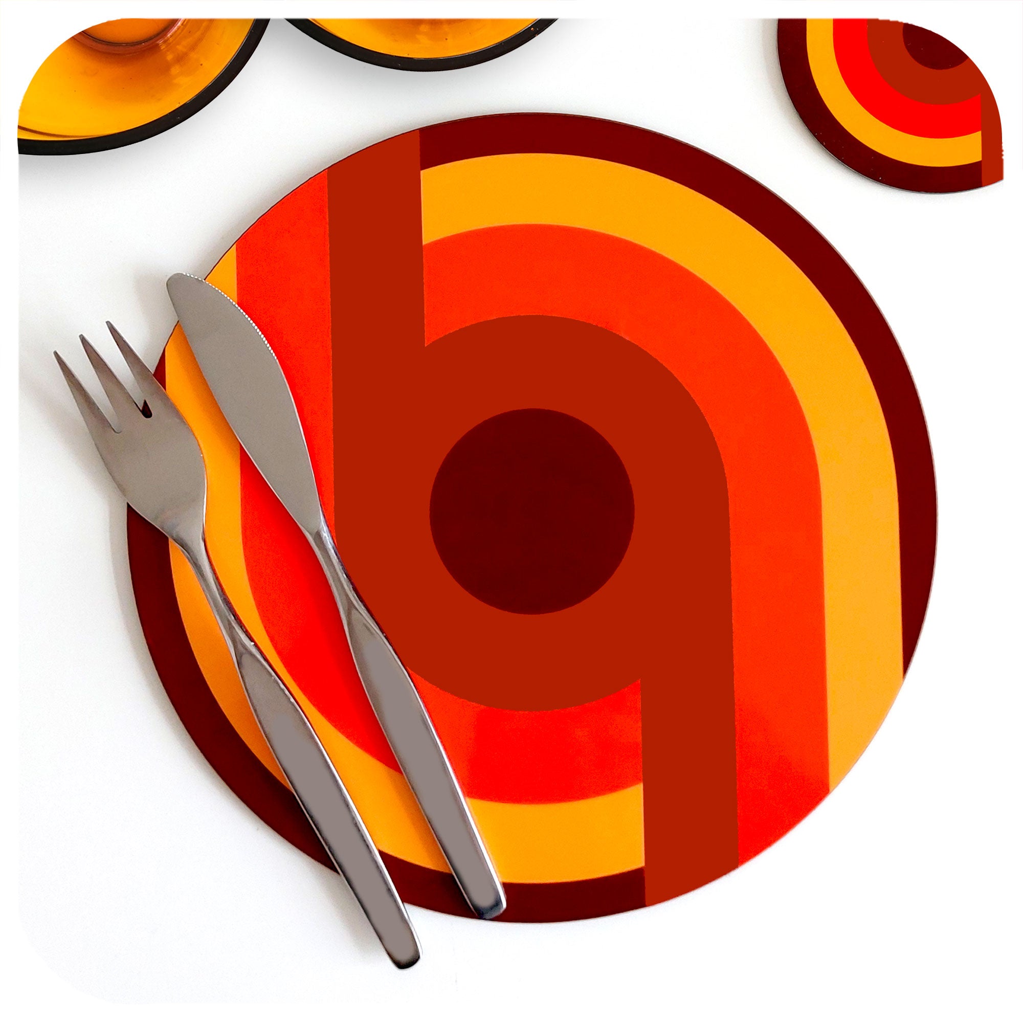 70s Supergraphic style round placemat on a white table with vintage mid century knife and fork, and 70s glass bowls and coaster just visible on edge of shot | The Inkabilly Emporium