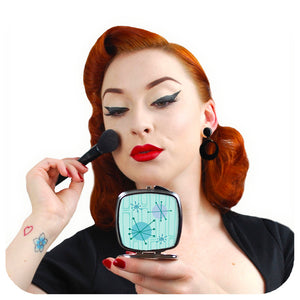 Head & shoulders sot of Vintage Pin-up model Miss Jessica Holly applying make-up while looking at herself  using Inkabilly's Atomic Starburst Compact Mirror