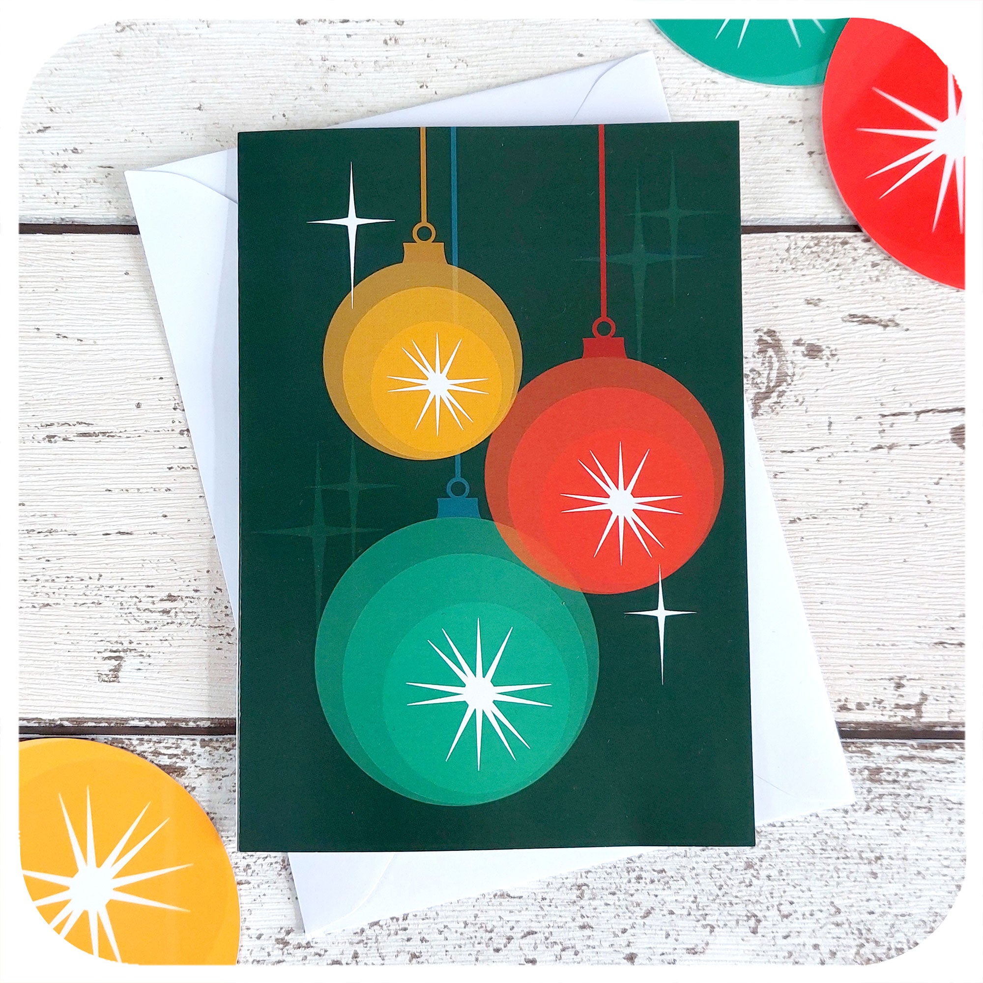 Mid Century style Christmas Card featuring 3 retro Christmas baubles and atomic style starbursts, with a white envelope, on a white table with 50s style xmas decorations | The Inkabilly Emporium